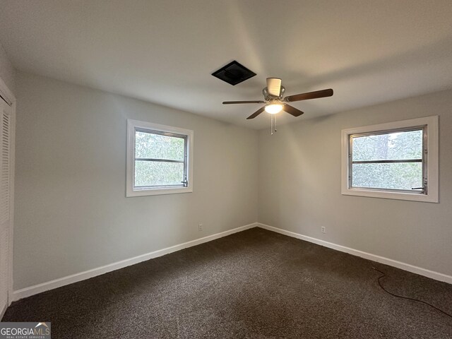 spare room featuring a wealth of natural light, a ceiling fan, baseboards, and dark colored carpet