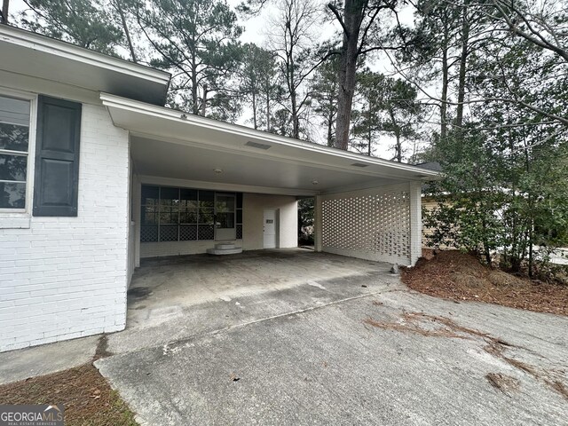 view of side of property featuring a carport, concrete driveway, and brick siding