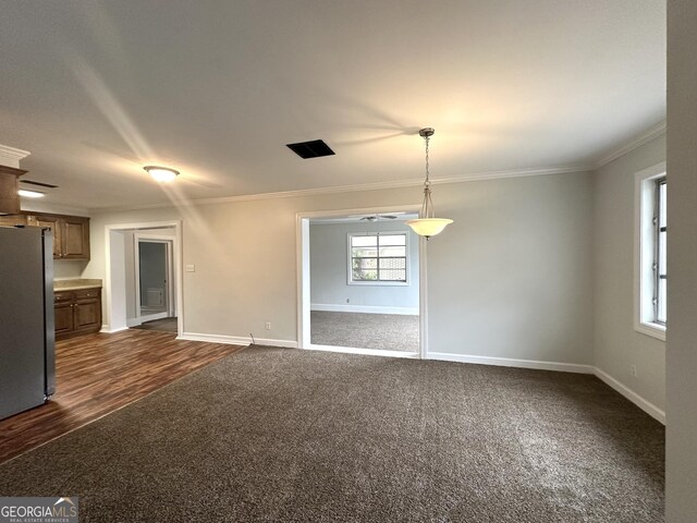 unfurnished living room with baseboards, ornamental molding, and dark carpet