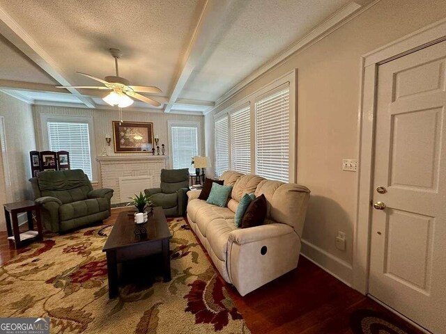 living room with a stone fireplace, beamed ceiling, wood-type flooring, a textured ceiling, and ceiling fan