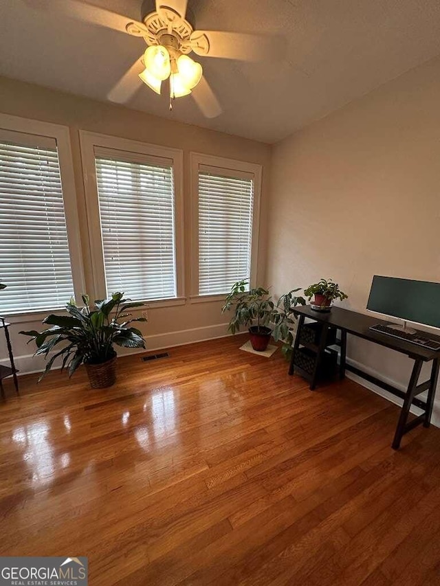 living area with ceiling fan, a wealth of natural light, and hardwood / wood-style flooring