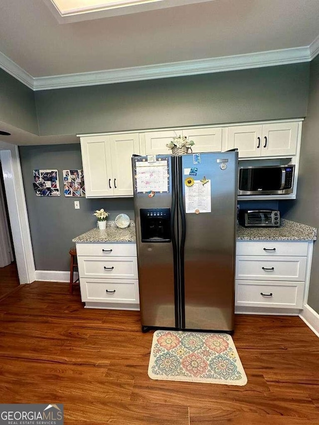 kitchen with white cabinets, ornamental molding, appliances with stainless steel finishes, light stone countertops, and dark wood finished floors