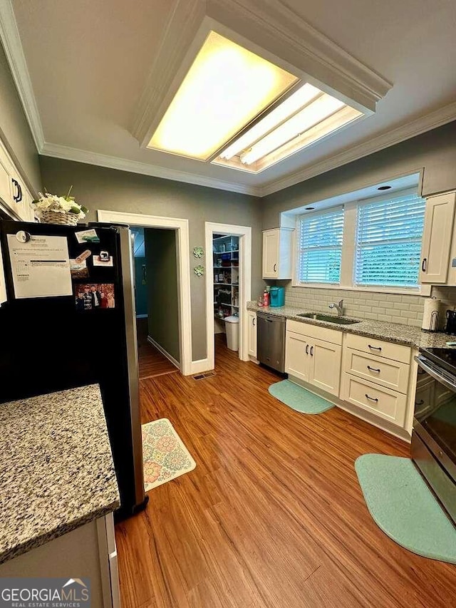 kitchen featuring stainless steel appliances, light wood-style flooring, ornamental molding, white cabinets, and a sink