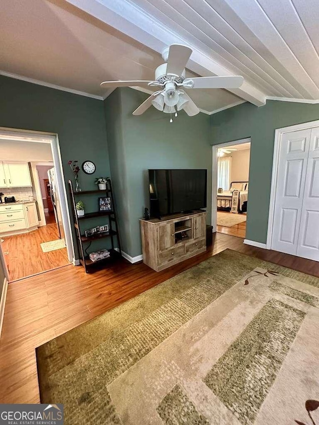 living room with beamed ceiling, crown molding, wood-type flooring, and ceiling fan