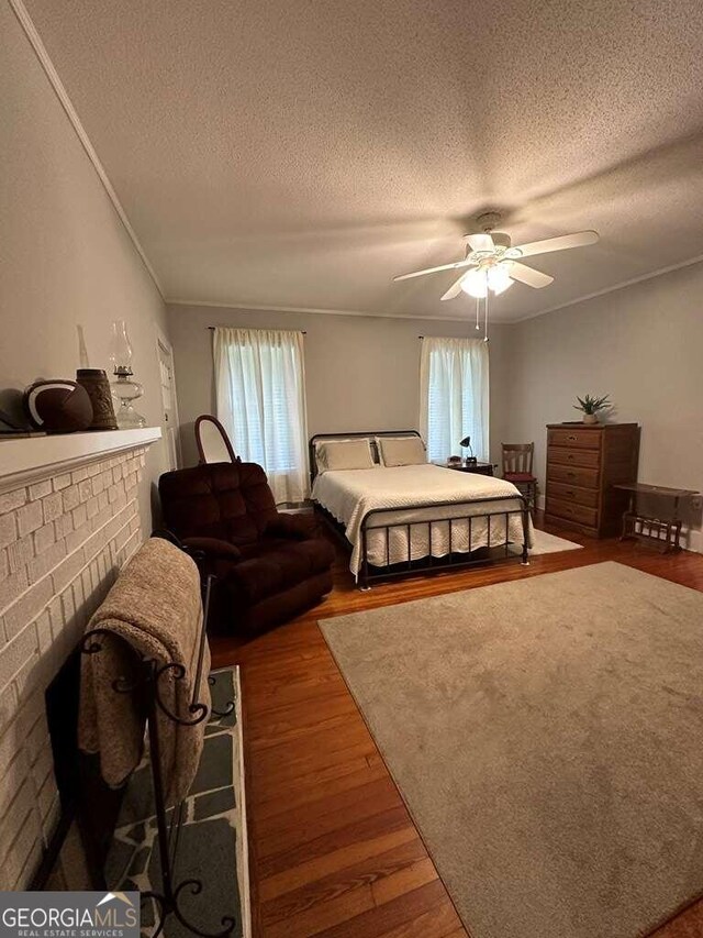 bedroom featuring ceiling fan, hardwood / wood-style flooring, a textured ceiling, and a fireplace