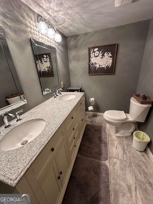 bathroom with toilet, double vanity, baseboards, and a sink