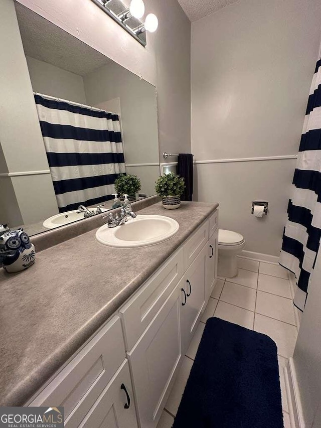 bathroom featuring a textured ceiling, tile patterned flooring, toilet, vanity, and baseboards