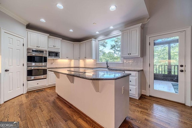 kitchen featuring dark wood-type flooring, a healthy amount of sunlight, a kitchen island, white cabinetry, and stainless steel appliances