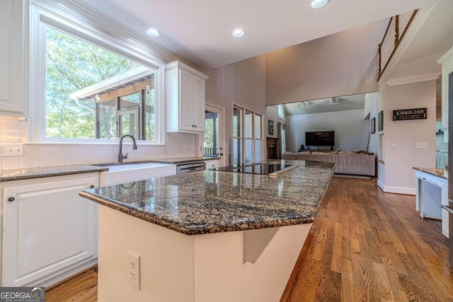 kitchen with backsplash, sink, white cabinets, wood-type flooring, and a center island