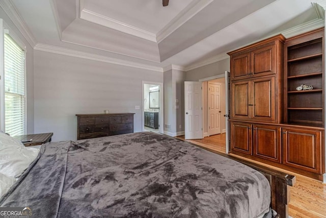 bedroom with a tray ceiling, light hardwood / wood-style floors, ornamental molding, and ensuite bath