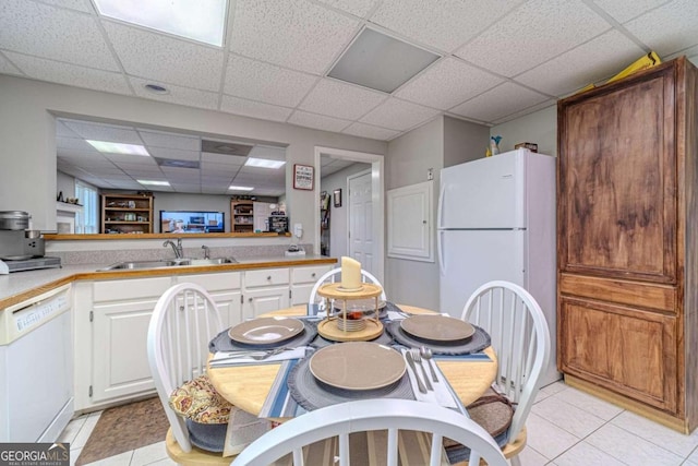 kitchen with a paneled ceiling, white cabinets, light tile patterned floors, sink, and white appliances