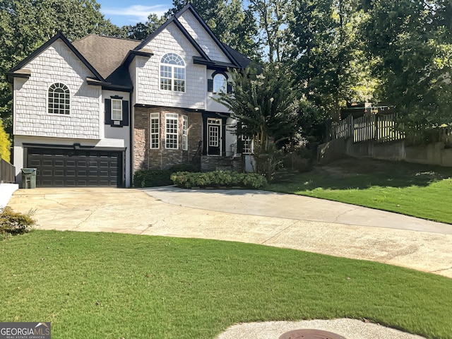 view of front of house with driveway, stone siding, an attached garage, fence, and a front lawn