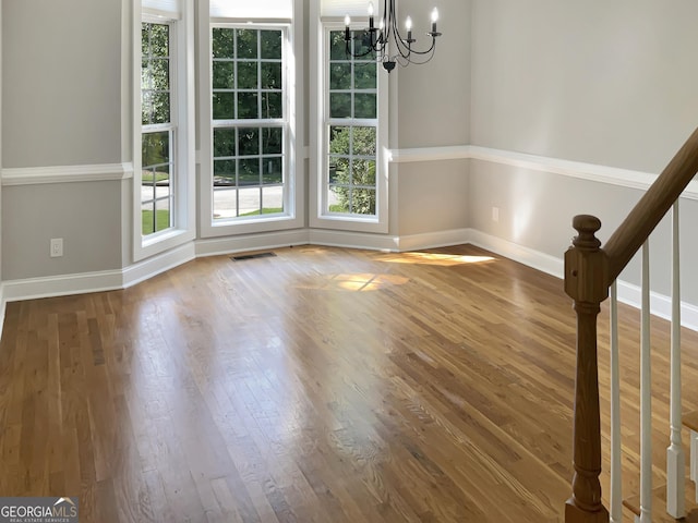 unfurnished dining area featuring visible vents, stairway, an inviting chandelier, wood finished floors, and baseboards