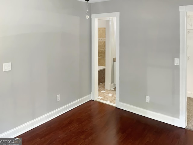 unfurnished bedroom with ensuite bathroom, baseboards, and wood finished floors