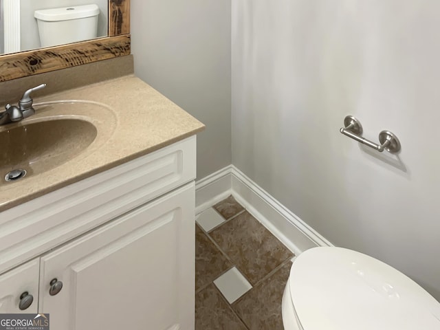 half bathroom with baseboards, vanity, toilet, and tile patterned floors