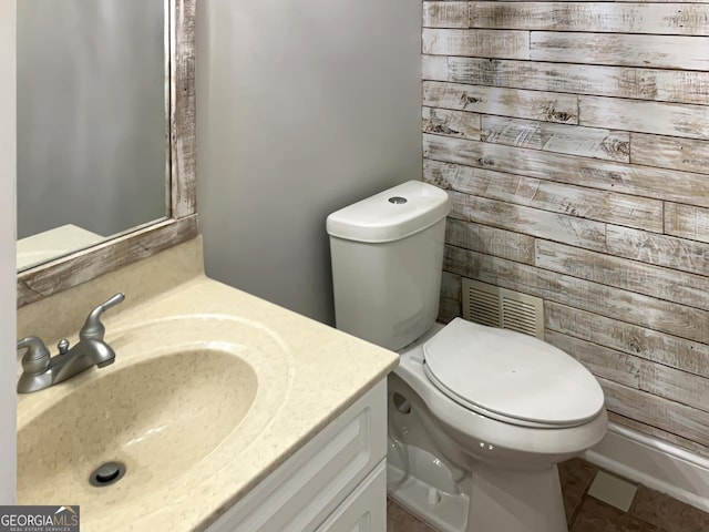 half bath with visible vents, wooden walls, toilet, and vanity