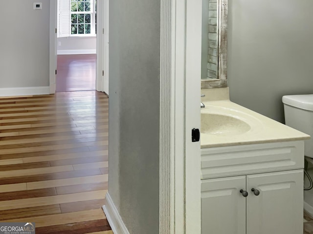 half bathroom featuring baseboards, vanity, toilet, and wood finished floors