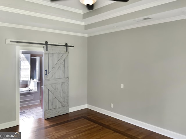 unfurnished room with a barn door, visible vents, dark wood finished floors, baseboards, and crown molding