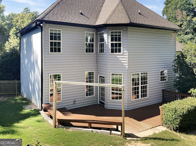 back of house with a shingled roof, a lawn, a deck, and fence