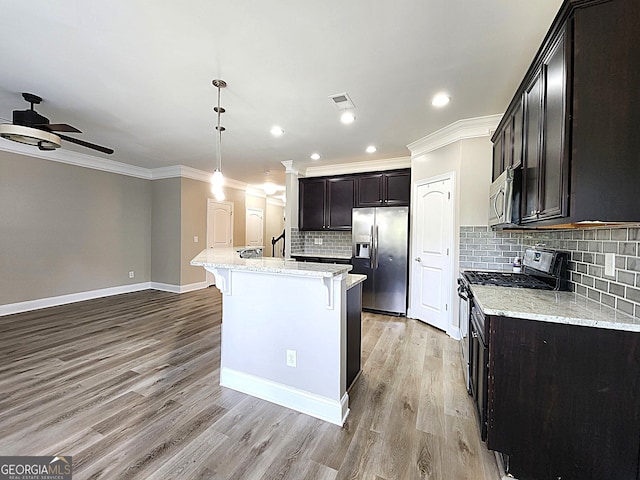 kitchen featuring ceiling fan, tasteful backsplash, appliances with stainless steel finishes, light hardwood / wood-style floors, and a center island with sink