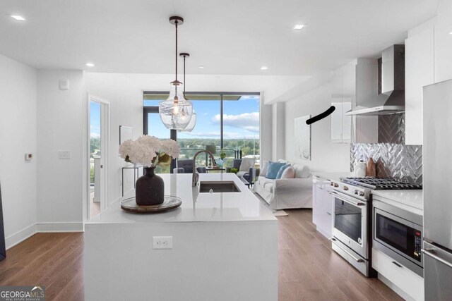 kitchen featuring backsplash, wall chimney exhaust hood, white cabinetry, hardwood / wood-style flooring, and stainless steel appliances