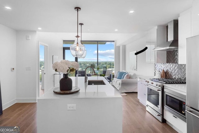 kitchen with stainless steel appliances, light countertops, wall chimney range hood, and an island with sink