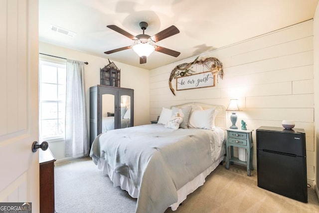 bedroom with ceiling fan, light carpet, and black refrigerator