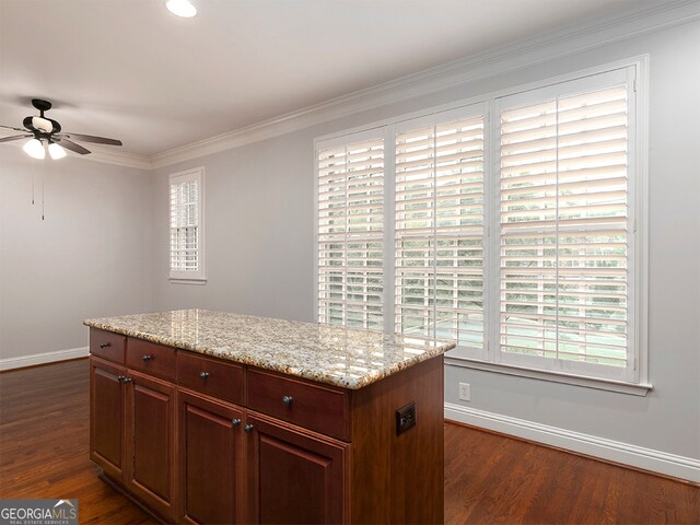 kitchen featuring ceiling fan, dark hardwood / wood-style floors, a center island, light stone countertops, and crown molding