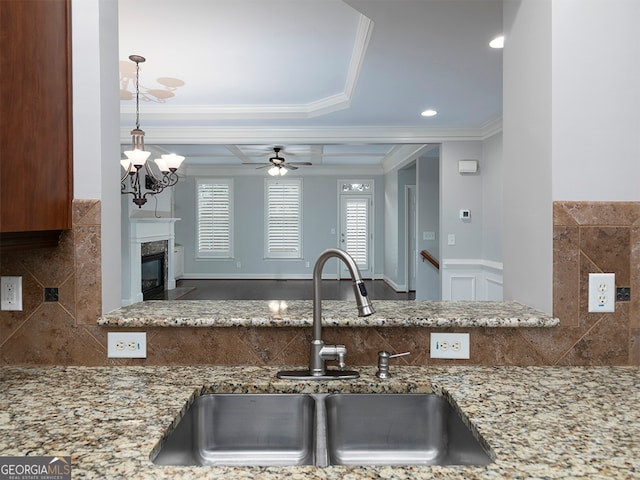 kitchen with ornamental molding, sink, stone counters, a fireplace, and ceiling fan with notable chandelier