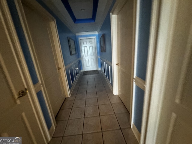 corridor with tile patterned flooring, a wainscoted wall, a decorative wall, and a tray ceiling