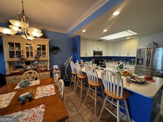 kitchen with tile patterned floors, light countertops, stainless steel appliances, crown molding, and white cabinetry