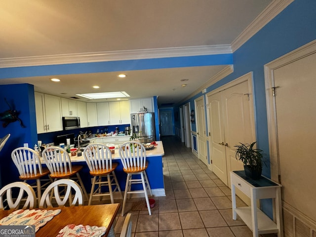 kitchen with stainless steel appliances, ornamental molding, white cabinetry, a peninsula, and tile patterned floors