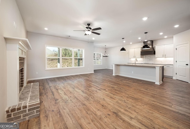 kitchen featuring pendant lighting, wall chimney range hood, sink, light wood-type flooring, and stainless steel appliances