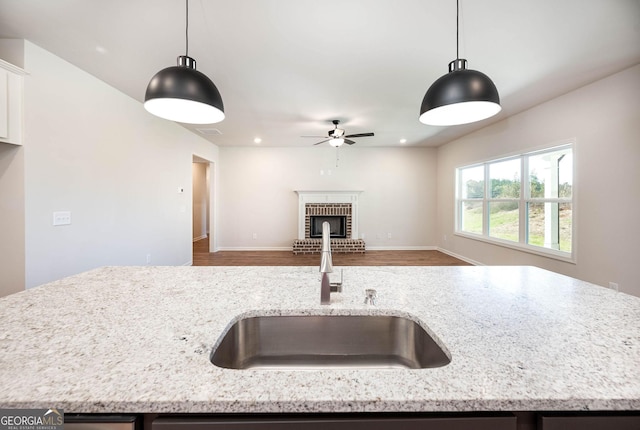 kitchen with wood-type flooring, decorative light fixtures, light stone counters, and sink