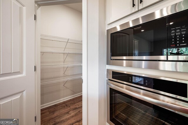 kitchen with premium range hood, white cabinets, oven, sink, and an island with sink