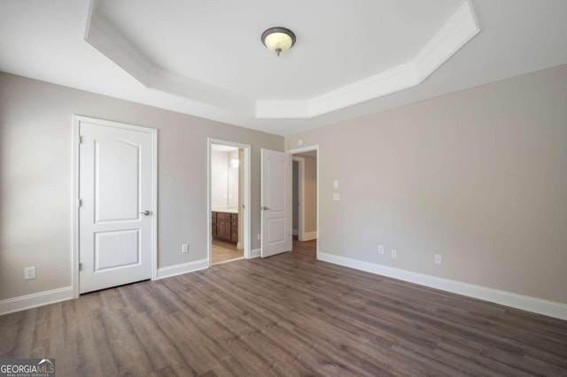 unfurnished bedroom with dark hardwood / wood-style floors, connected bathroom, and a tray ceiling