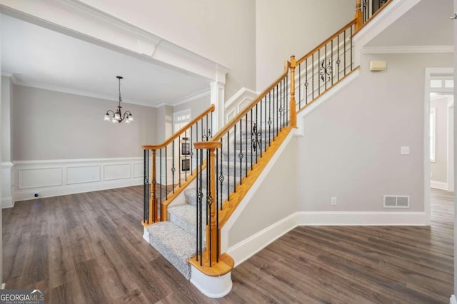 stairway with hardwood / wood-style flooring, crown molding, decorative columns, and a chandelier