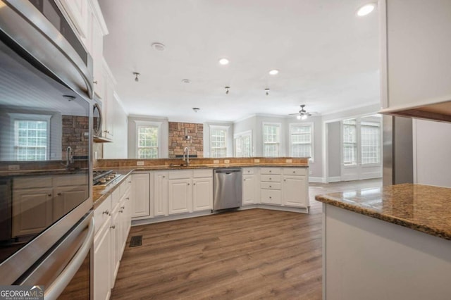 kitchen with white cabinets, kitchen peninsula, appliances with stainless steel finishes, and hardwood / wood-style floors