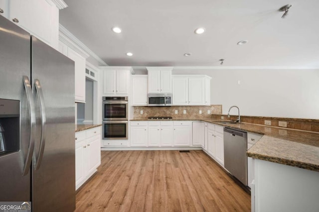 kitchen featuring appliances with stainless steel finishes, light hardwood / wood-style flooring, sink, dark stone counters, and kitchen peninsula