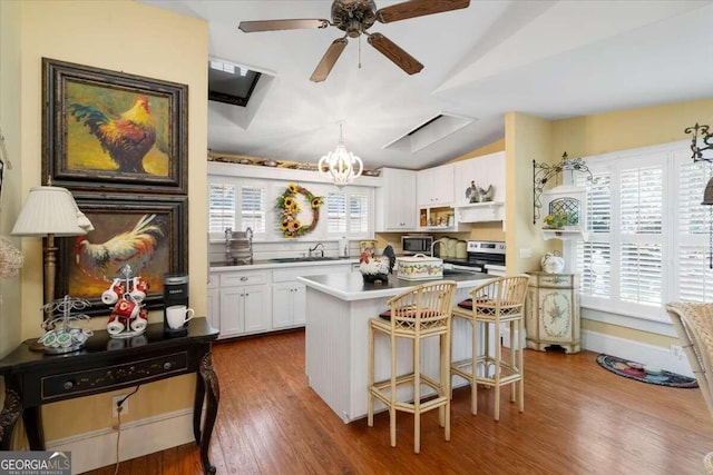 kitchen featuring appliances with stainless steel finishes, white cabinetry, a kitchen bar, a kitchen island, and hardwood / wood-style flooring