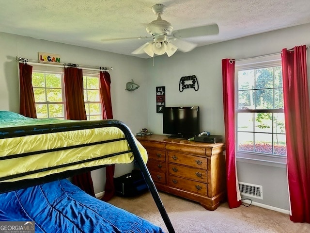 carpeted bedroom featuring a textured ceiling, ceiling fan, and multiple windows