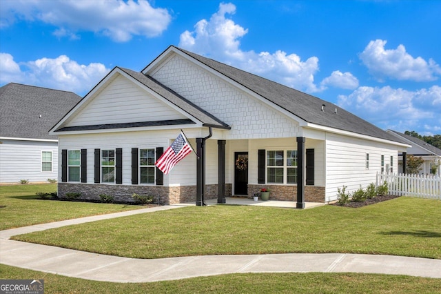 craftsman-style home featuring a shingled roof, stone siding, fence, and a front lawn