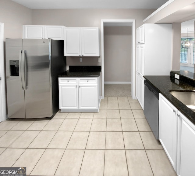 kitchen featuring light tile patterned floors, stainless steel appliances, a sink, white cabinets, and dark stone countertops