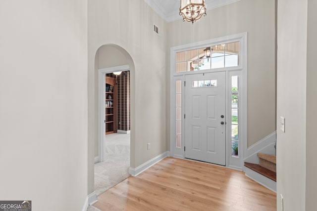 foyer entrance featuring ornamental molding, a chandelier, light hardwood / wood-style flooring, and a high ceiling