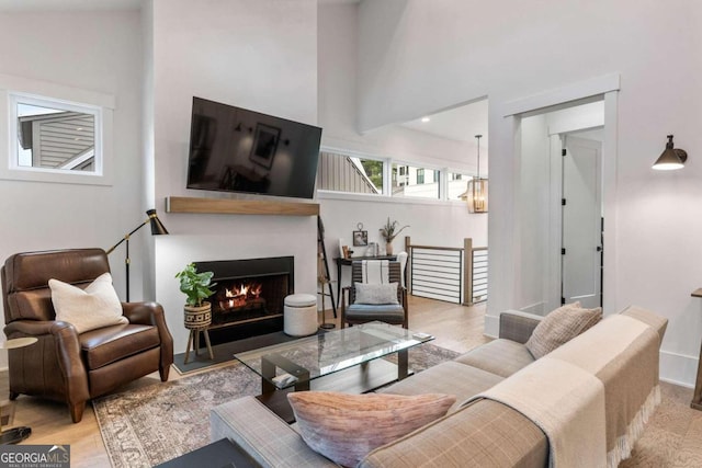 living area with baseboards, a high ceiling, a lit fireplace, and wood finished floors