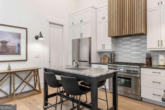 kitchen with baseboards, custom exhaust hood, light wood-style flooring, decorative backsplash, and appliances with stainless steel finishes