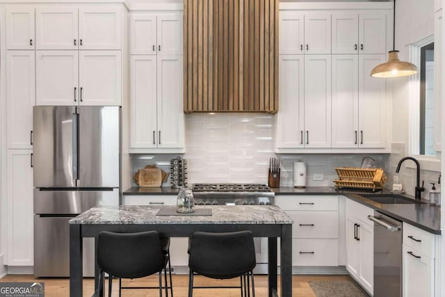 kitchen featuring backsplash, appliances with stainless steel finishes, a kitchen breakfast bar, white cabinetry, and a sink