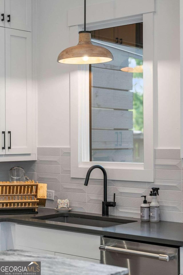 kitchen featuring a sink, stainless steel dishwasher, dark countertops, white cabinetry, and decorative backsplash