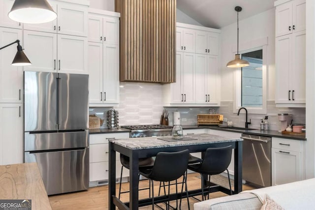 kitchen with light wood finished floors, backsplash, vaulted ceiling, stainless steel appliances, and a sink