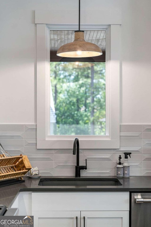 kitchen featuring dark countertops, backsplash, white cabinetry, and a sink